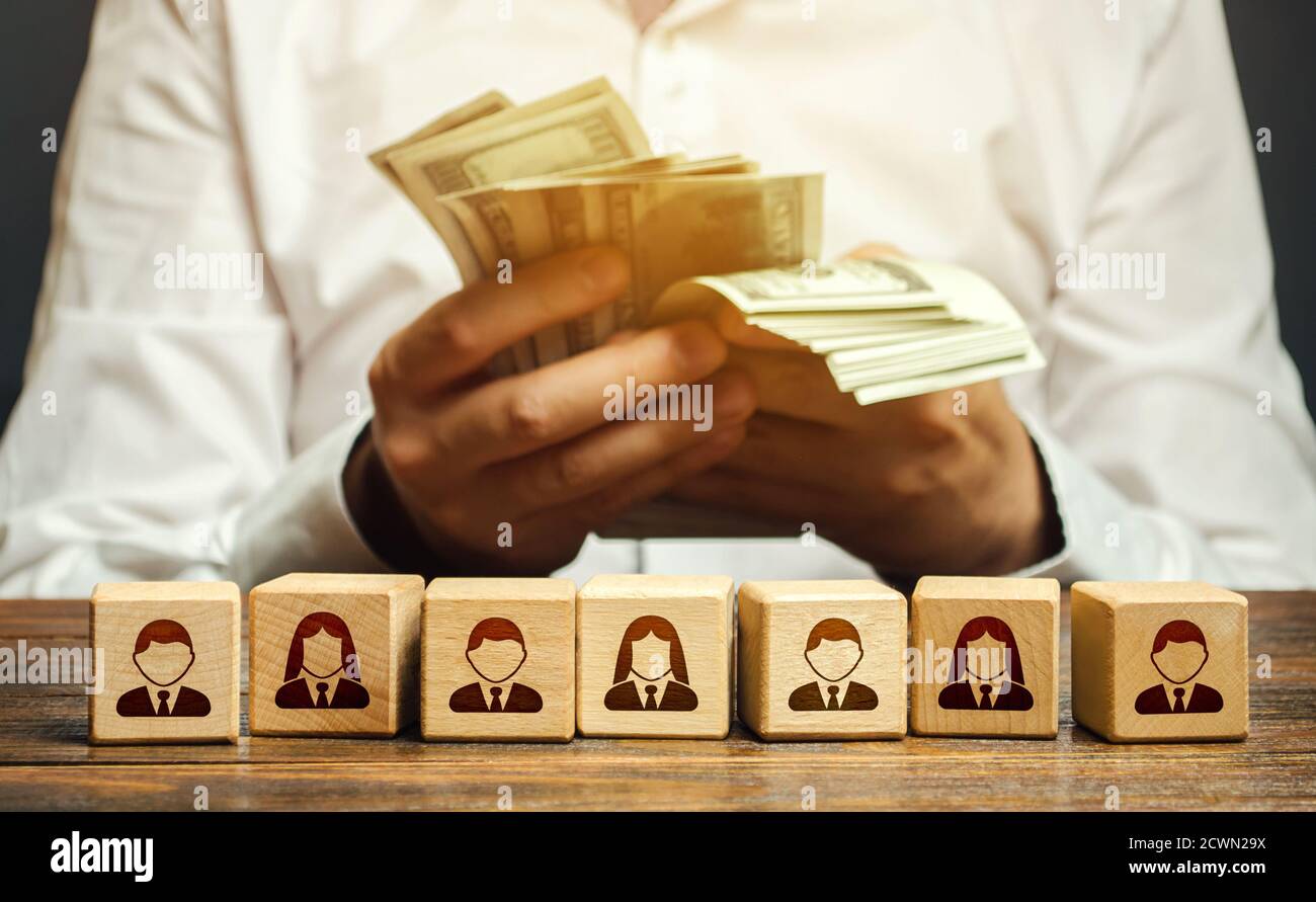 Ein Mann zählt Geld in seinen Händen über Blöcke mit Symbolen der Mitarbeiter. Lohnfonds. Rechnungslegung und Budgetierung. Zahltag. Ausbau einer profitablen Busine Stockfoto