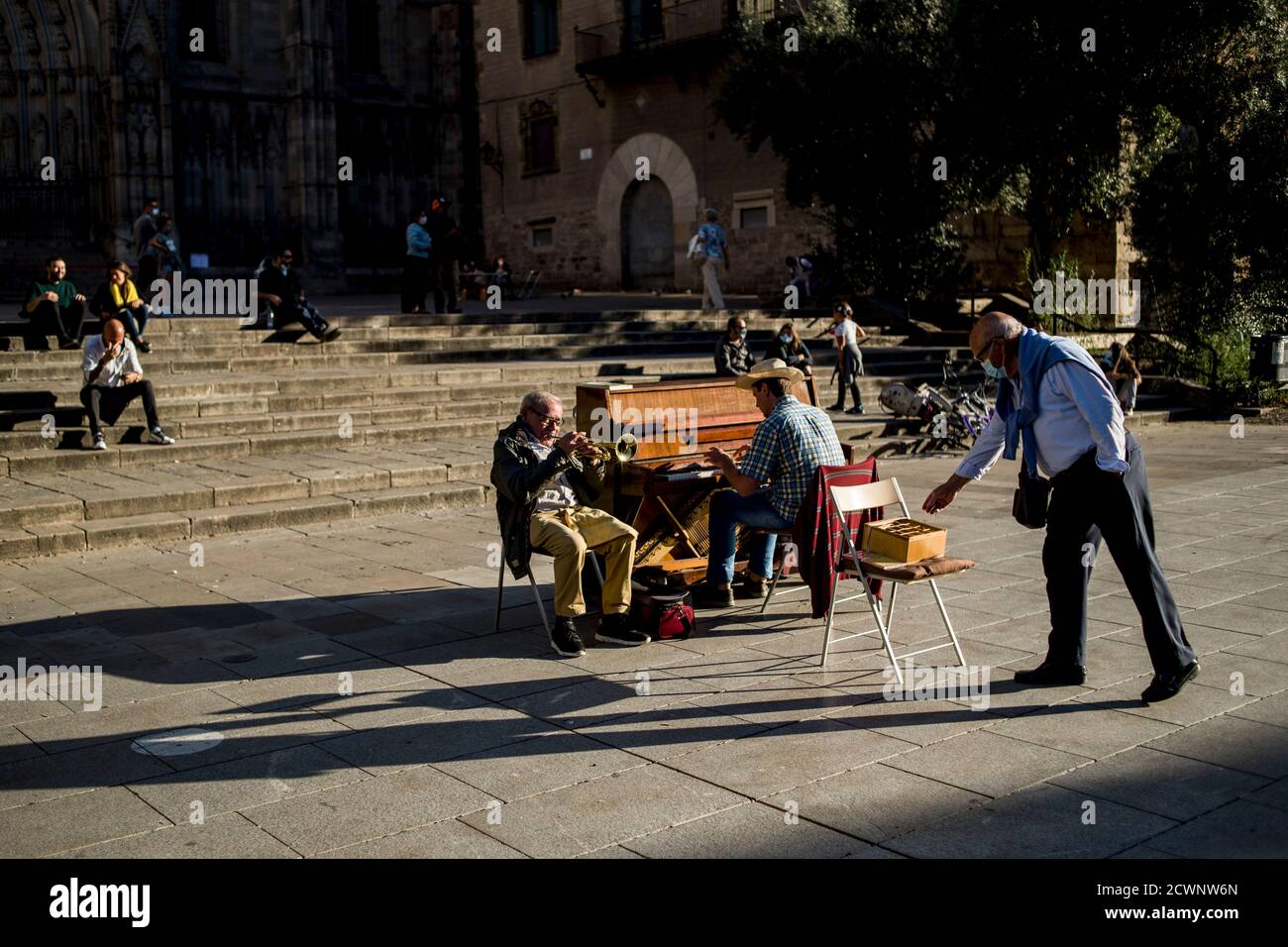 In Barcelona gibt ein Mann, der eine Gesichtsmaske trägt, um die Ausbreitung des Coronavirus zu verhindern, den performenden Straßenmusikern Münzen. Stockfoto