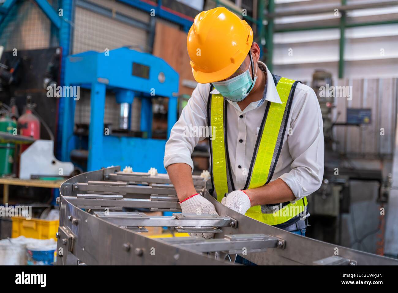 Asian Mann Mechanic Tragen Schutzmaske gegen Covid-19, männlich zu schützen Techniker Arbeiter arbeiten und montieren das Produkt Sortiermaschine Förderband Stockfoto