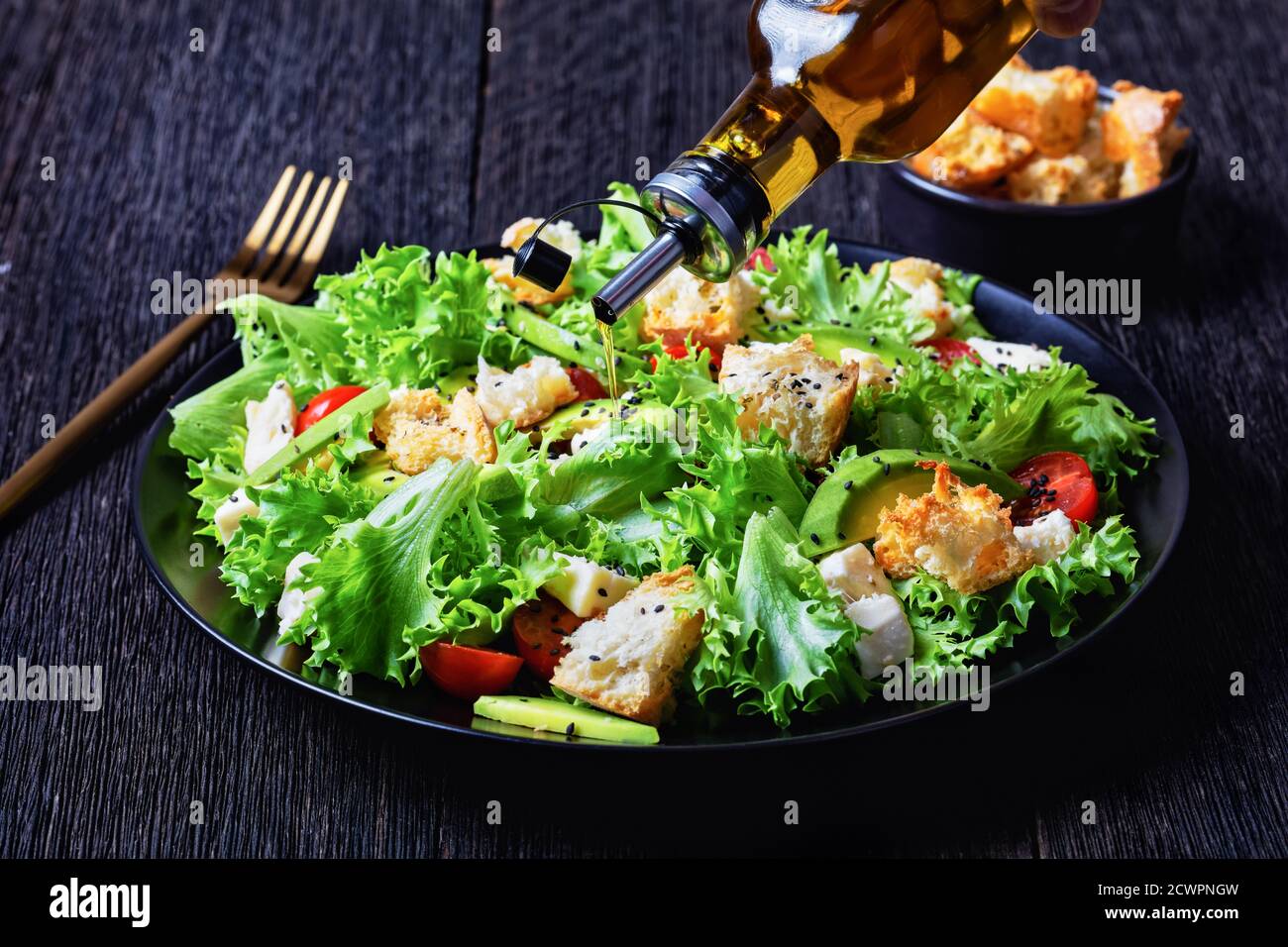 Nahaufnahme von Blattsalat mit Avocado, Kirschtomaten, Mozzarella und Croutons bestreut mit schwarzen Sesamsamen auf einem Teller, auf einem Holztisch, Mozzarella Stockfoto