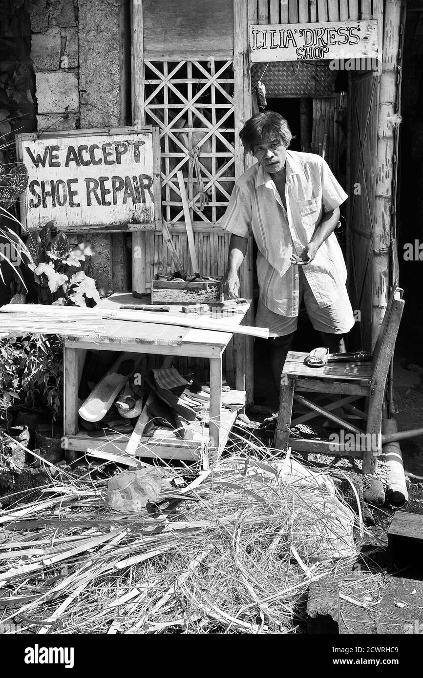 Älterer männlicher Besitzer eines Schuhreparatur- und Kleiderladens, der vor seinem Haus steht und Kunsthandwerk mit Bambus für seinen Lebensunterhalt macht, Philippinen, Asien Stockfoto
