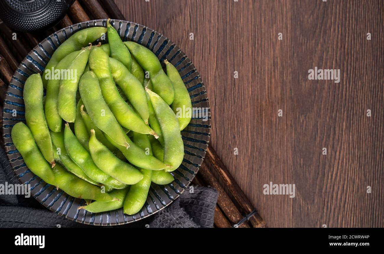 Frisch gekochte gekochte Edamame in einem Teller auf Holztablett und Tischhintergrund, Protein-Food-Konzept. Stockfoto