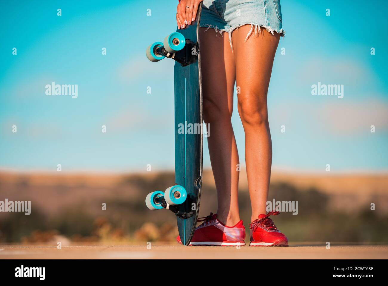 Fit female mit Skinny gebräunten Beinen in stilvollen Jeans Shorts Hält Skateboard Stockfoto