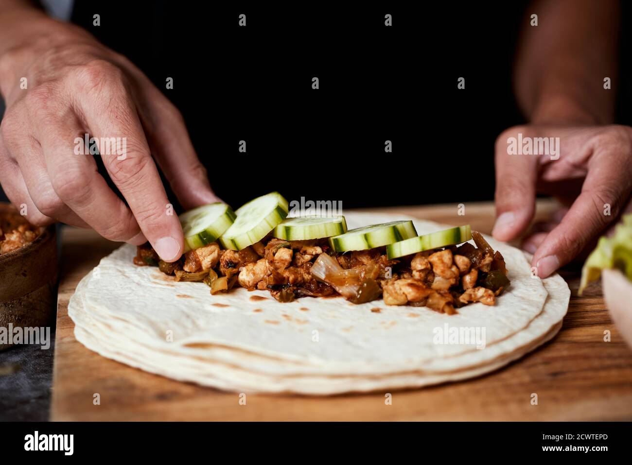 Nahaufnahme eines jungen kaukasischen Mannes, der ein Durum oder einen Burrito zubereitet, mit Hühnerfleisch, das mit verschiedenen Gemüsesorten wie Zwiebeln oder rotem und grünem Pep zubereitet wird Stockfoto