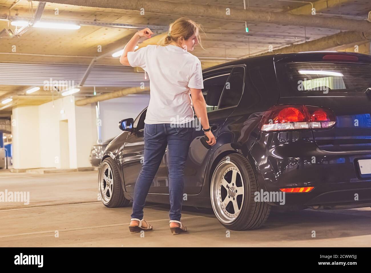 Abgeschwächt. Mädchen in einem weißen T-Shirt und Jeans poliert ihr Auto drinnen. Platz auf der Rückseite kopieren. Stockfoto