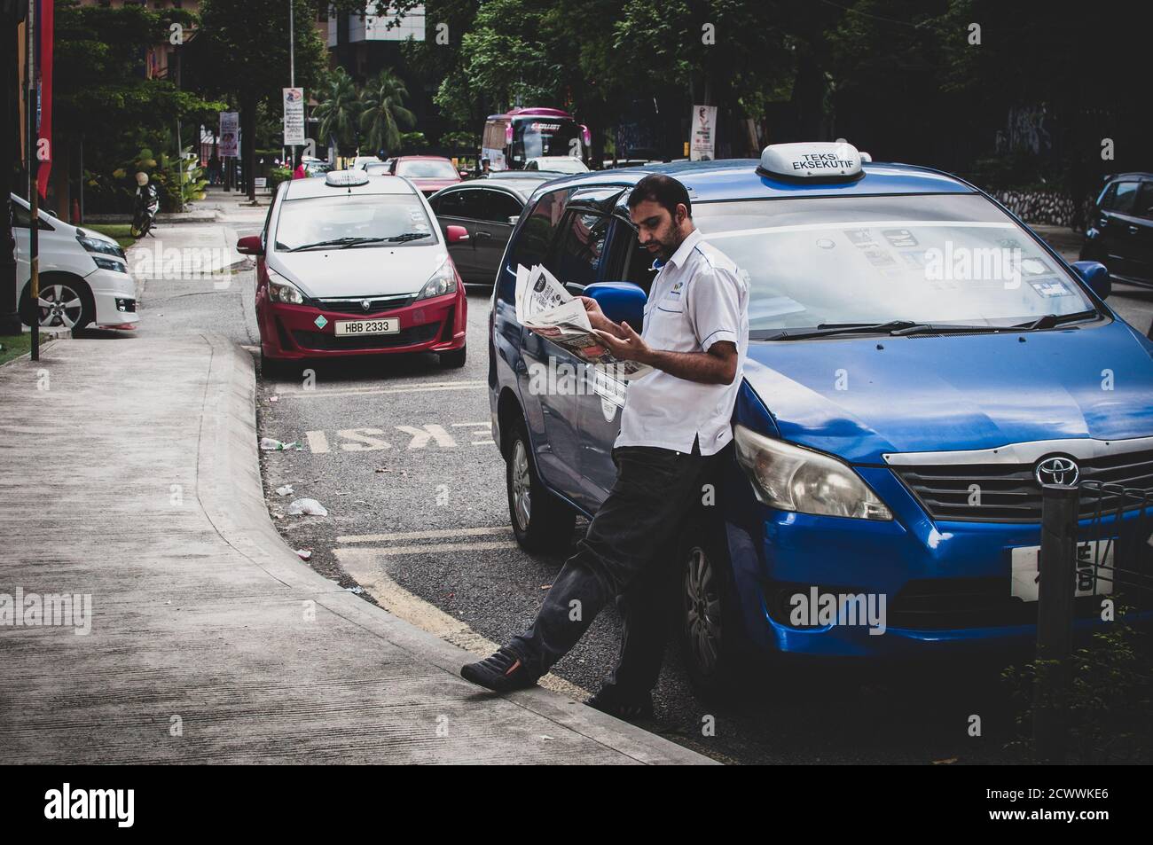 Asiatischer Taxifahrer, der vor seinem Auto hing und auf Kunden wartete Stockfoto