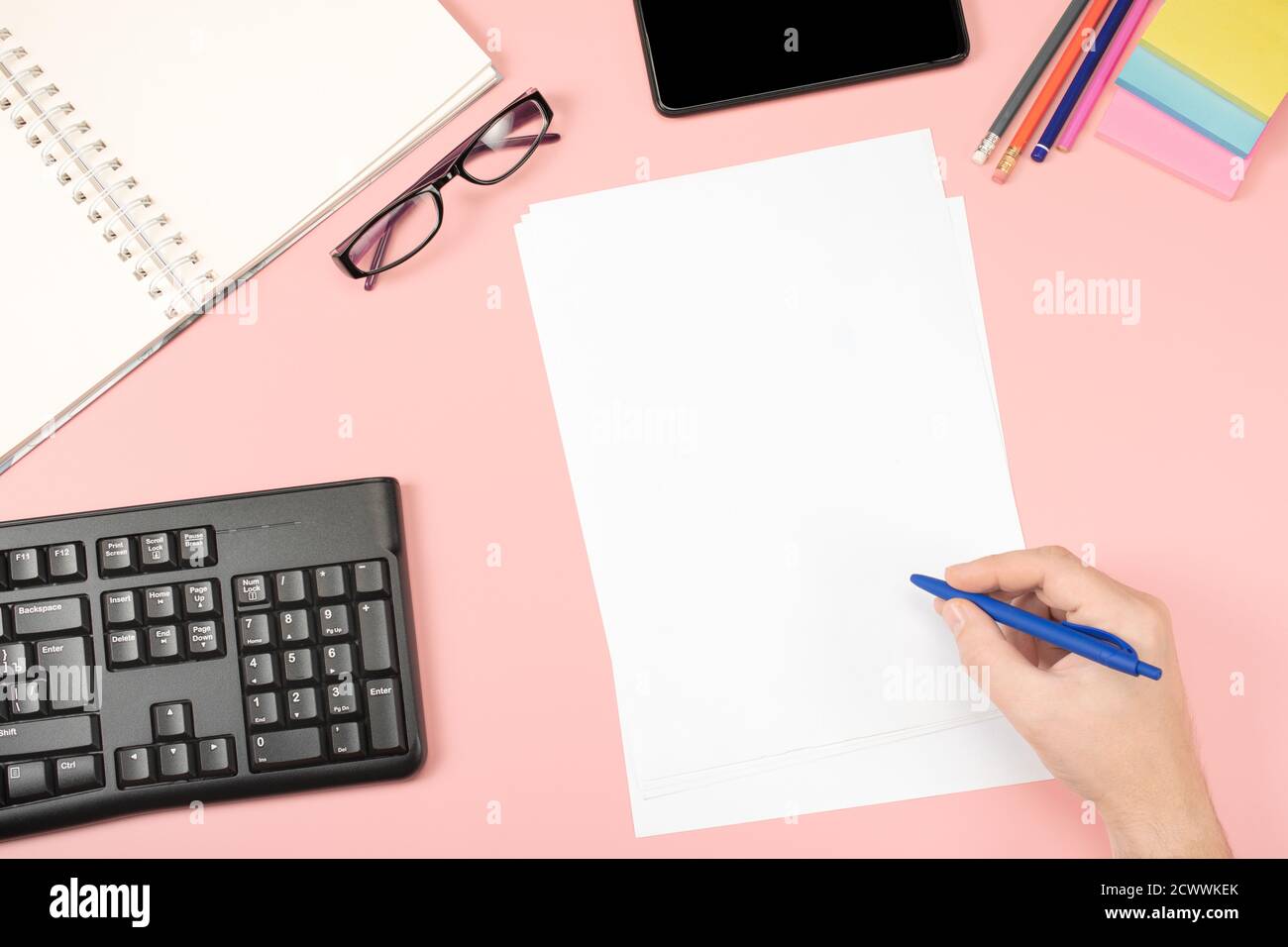 Weiße saubere Blätter für Unterlagen, Hand hält Stift, Bürobrille auf einem rosa Hintergrund. Flach liegend. Büroinhalt. Rosafarbener Tisch Stockfoto