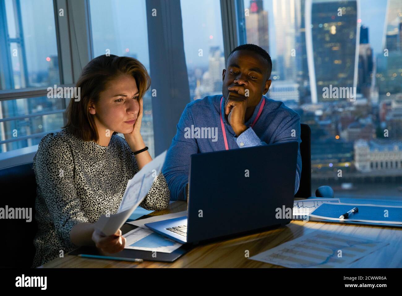 Geschäftsleute, die spät am Laptop im städtischen Hochhausbüro arbeiten Stockfoto