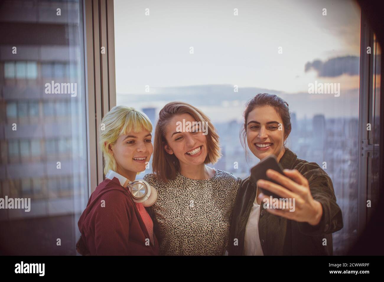 Lächelnde Geschäftsfrauen, die Selfie am Bürofenster im Hochhaus machen Stockfoto