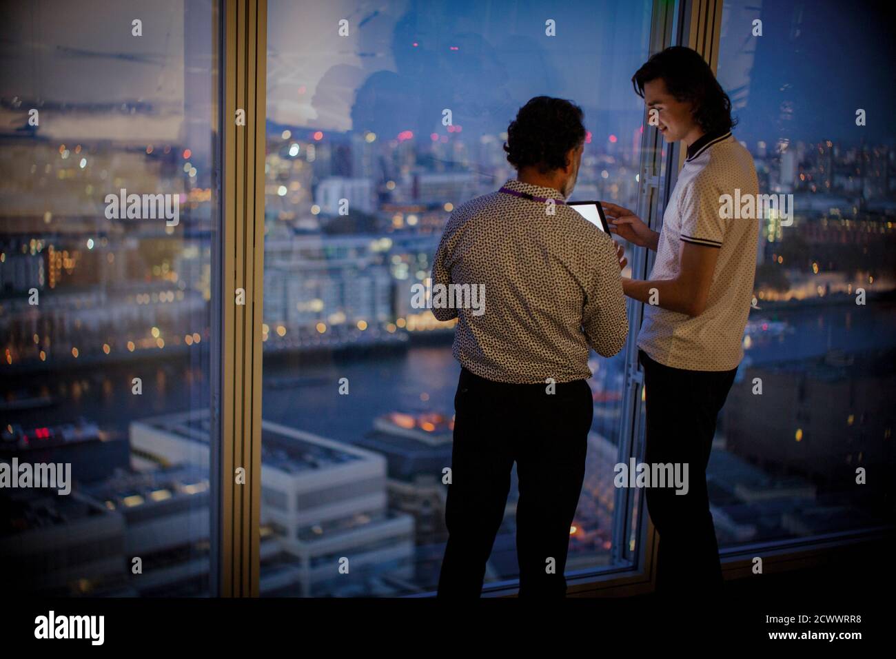 Geschäftsleute mit digitalem Tablet, die spät am Bürofenster im Hochhaus arbeiten Stockfoto