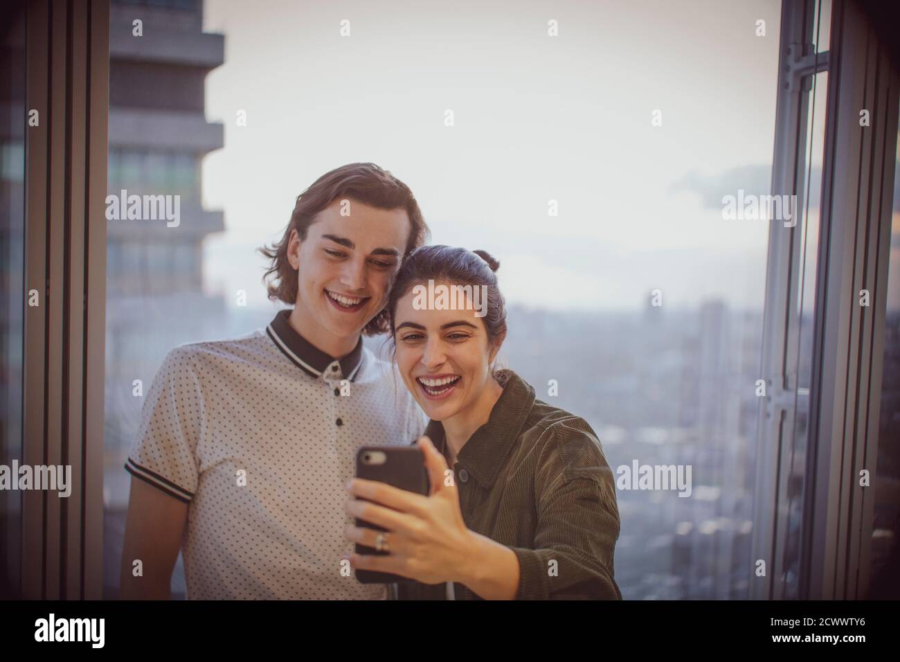 Glückliches junges Paar, das Selfie am Hochhausfenster nimmt Stockfoto