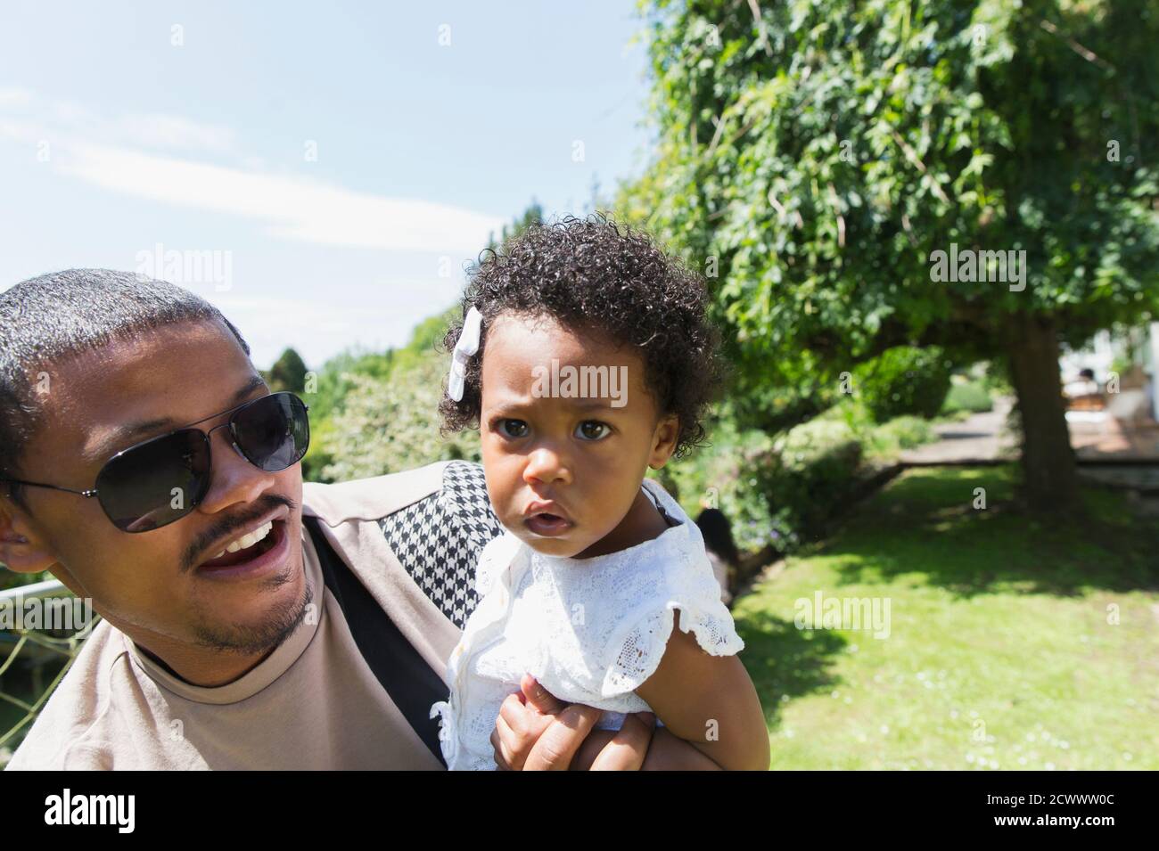Vater hält neugierige Kleinkind Tochter im sonnigen Sommer Hinterhof Stockfoto