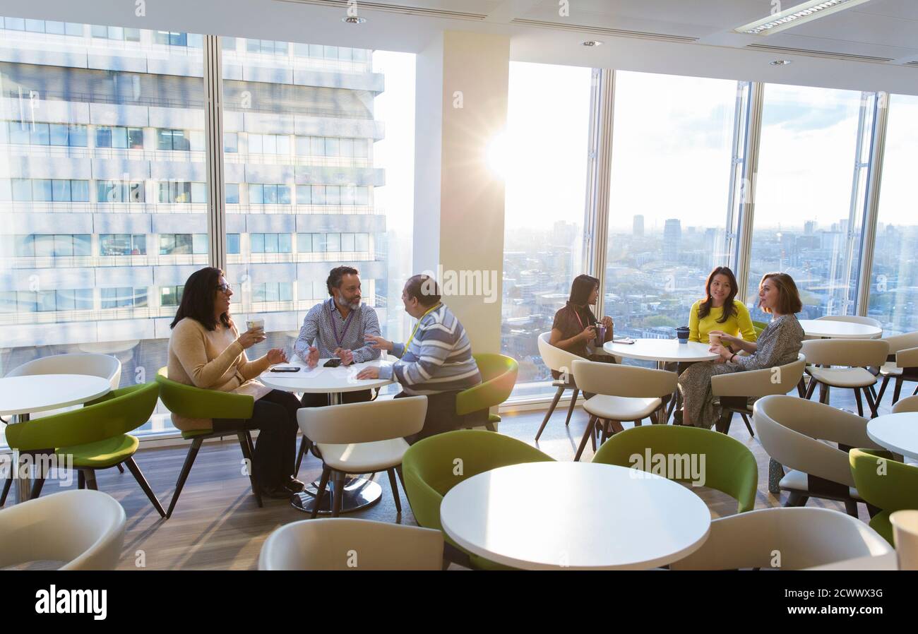 Geschäftsleute essen zu Mittag und unterhalten sich in der sonnigen Cafeteria in einem Hochhaus Stockfoto