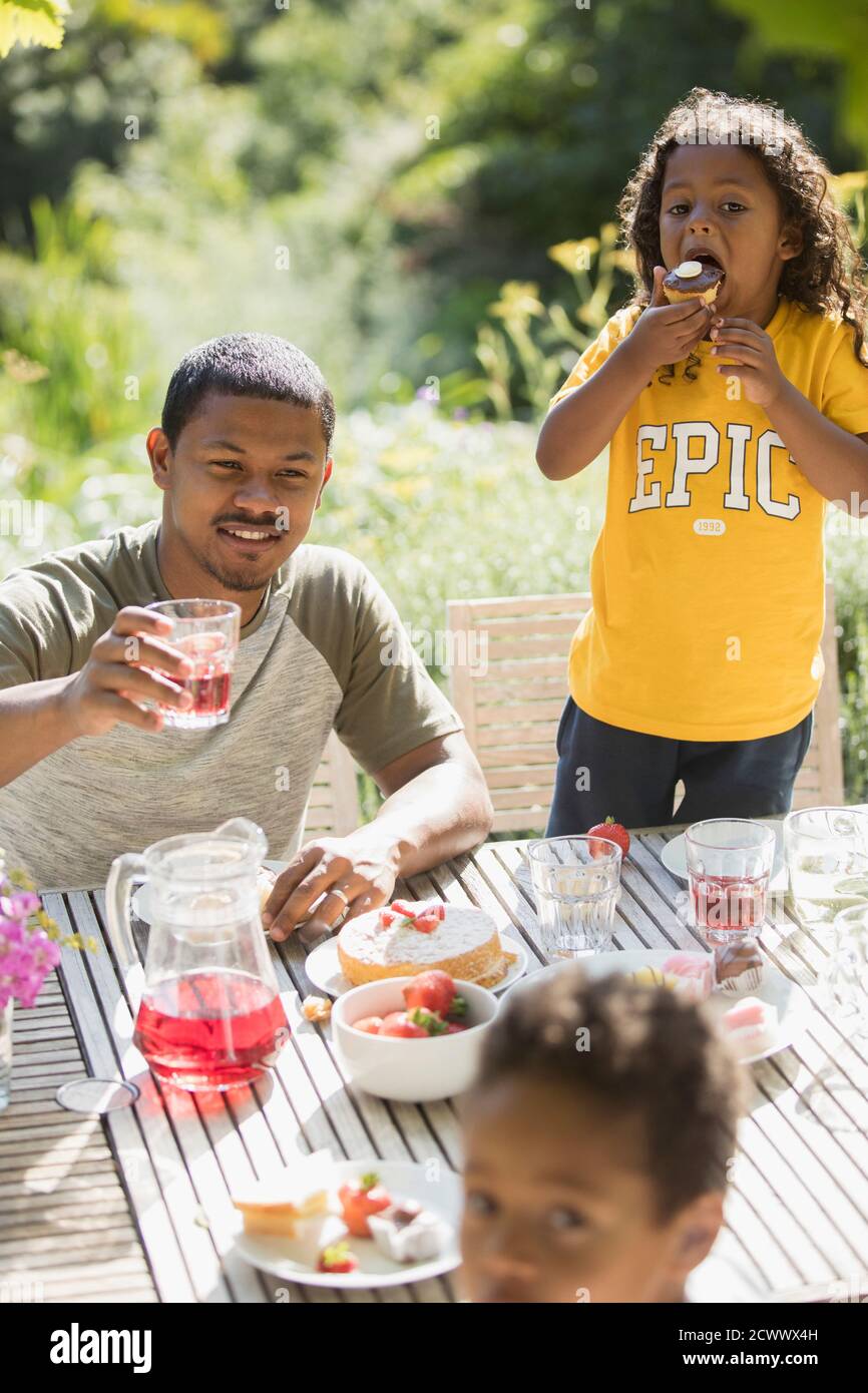 Vater und Kinder genießen Gartenessen auf sonniger Sommerterrasse Stockfoto