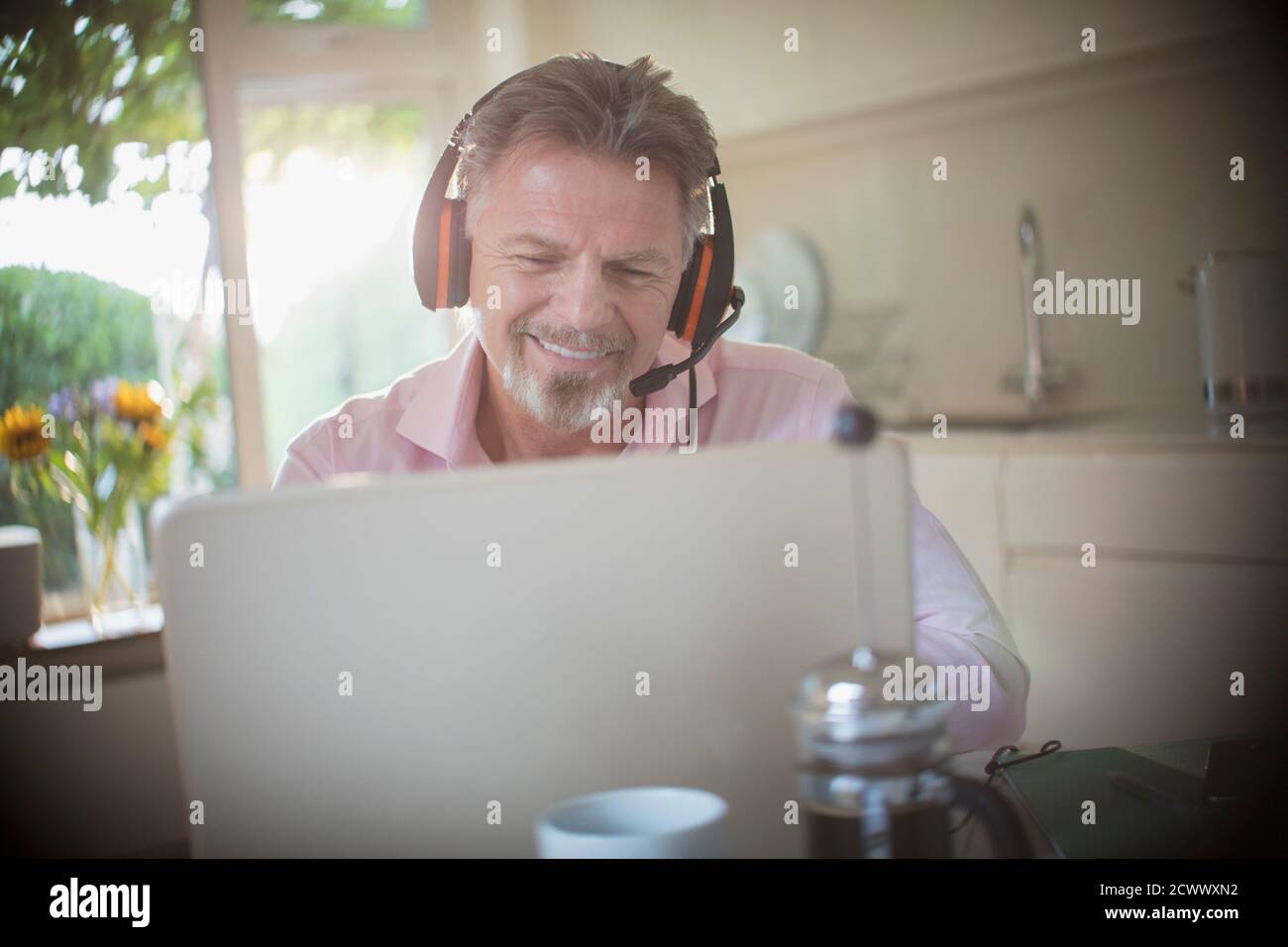 Ein glücklicher älterer Mann mit Kopfhörern, der morgens am Laptop arbeitete Küche Stockfoto