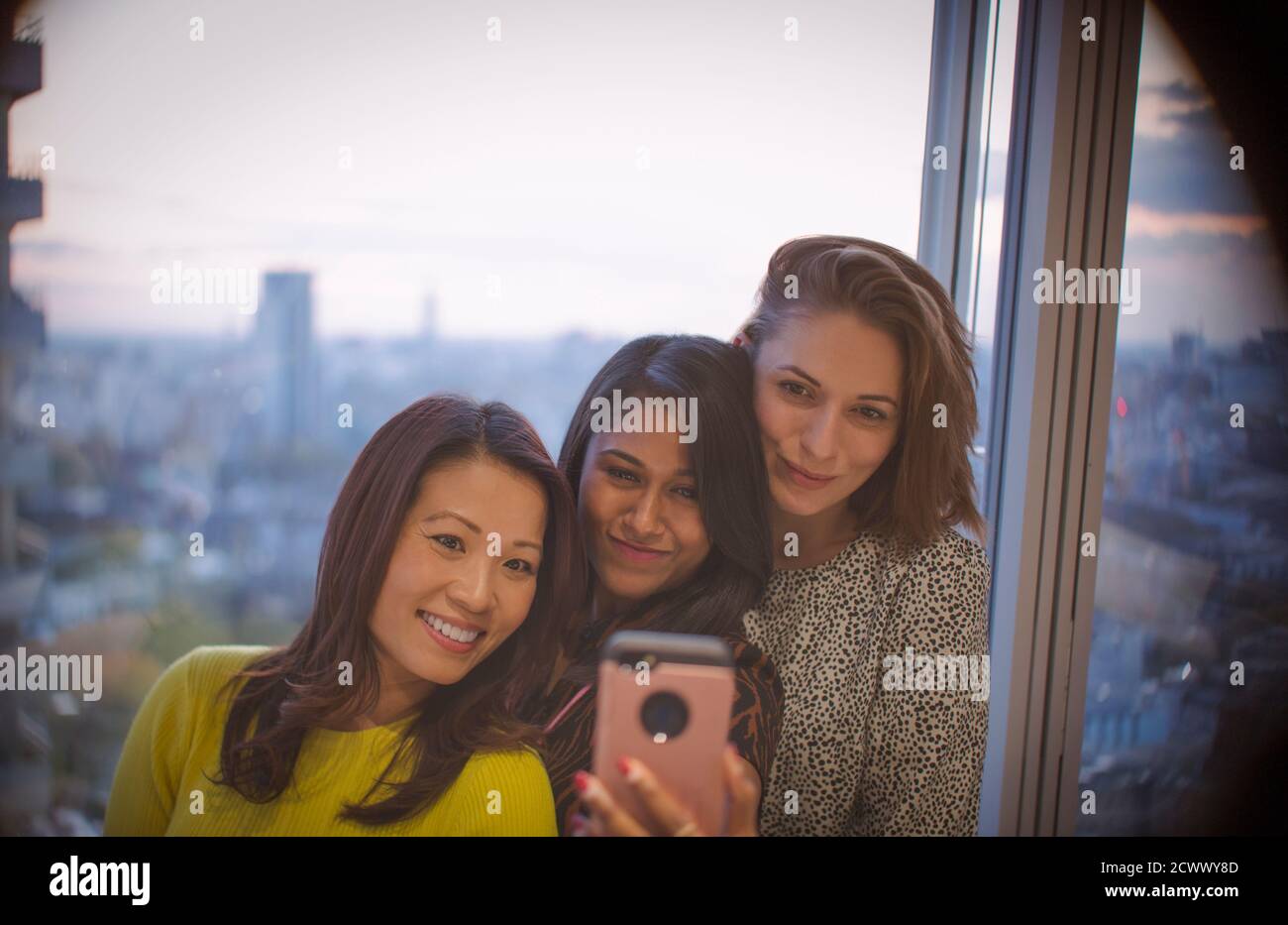 Geschäftsfrauen, die Selfie mit dem Smartphone am Bürofenster im Hochhaus machen Stockfoto