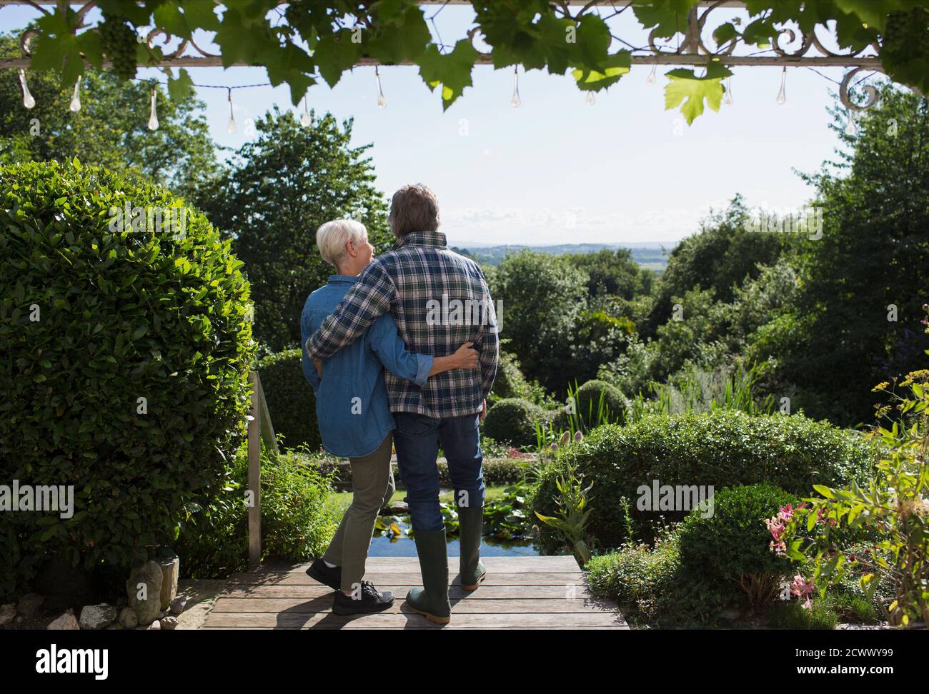 Liebevolles Seniorenpaar umarmt sich auf der sonnigen Sommerterrasse im Garten Stockfoto