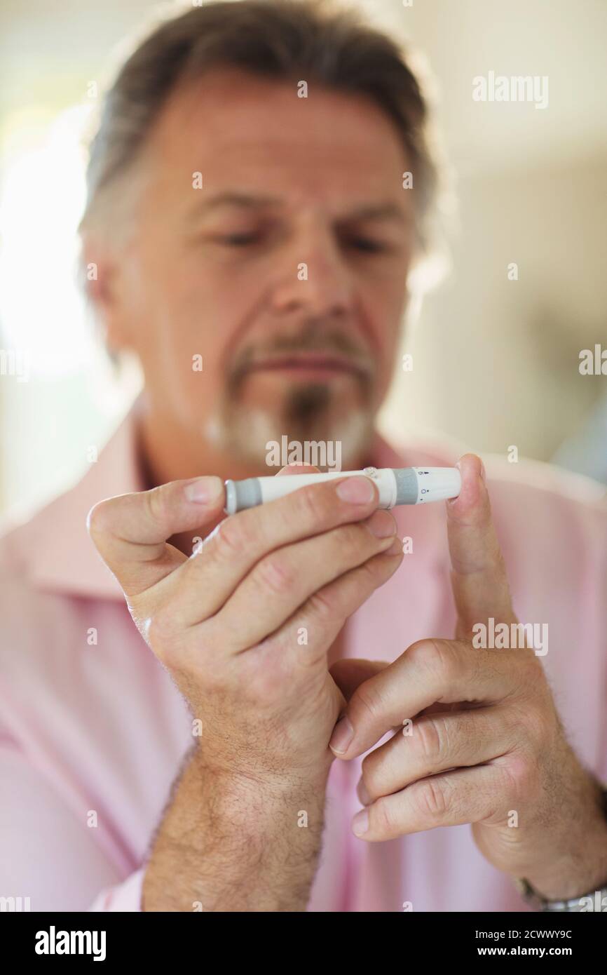 Älterer Mann mit Diabetes mit Blutzuckermessgerät am Finger Stockfoto