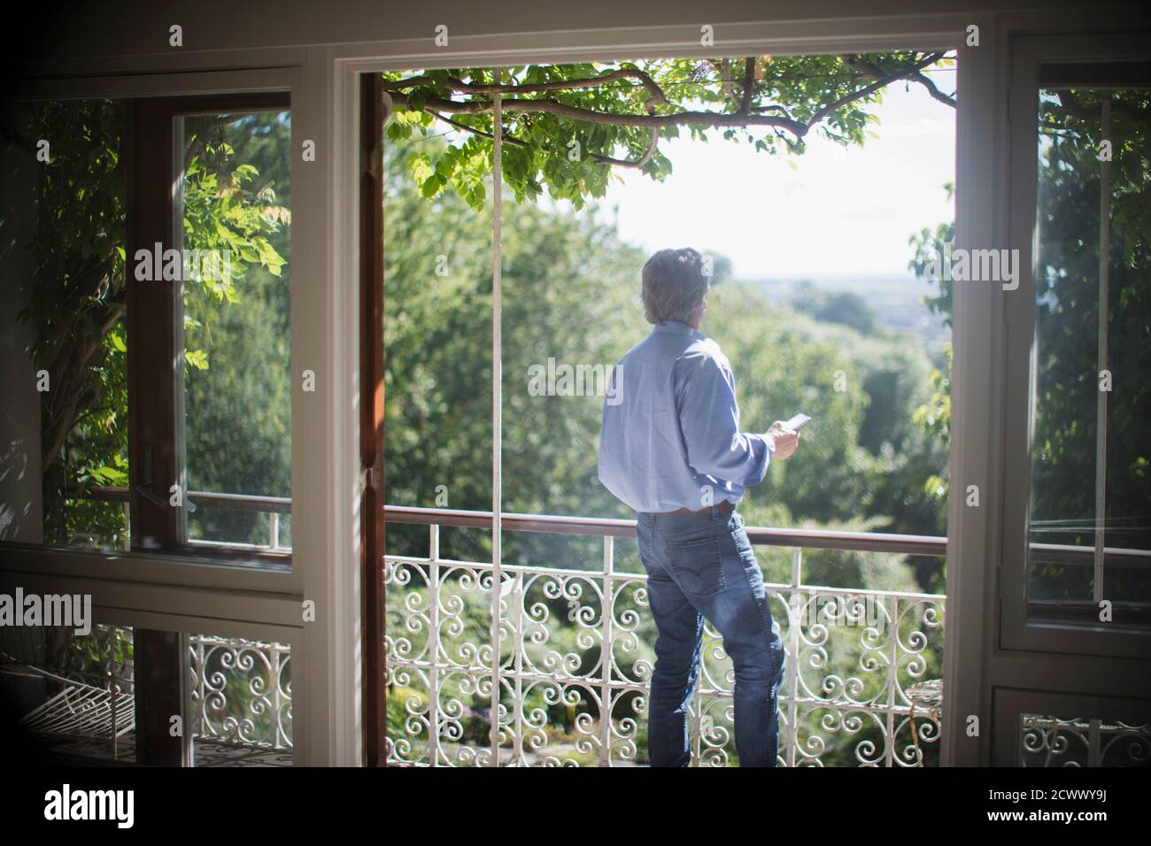 Älterer Mann mit Smartphone auf sonnigem, ruhigem Sommerbalkon Stockfoto