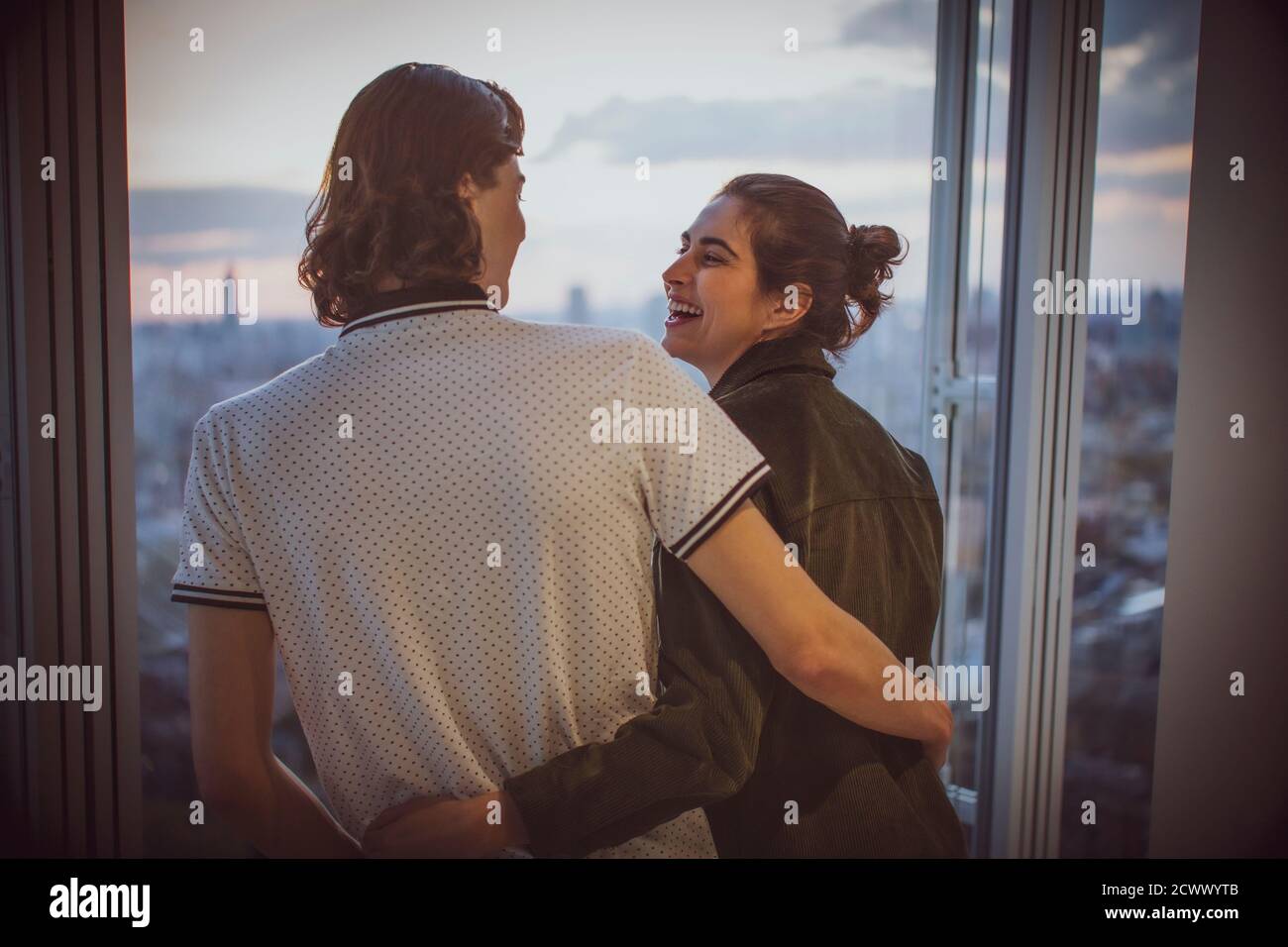 Glückliches junges Paar umarmt am Hochhausfenster Stockfoto