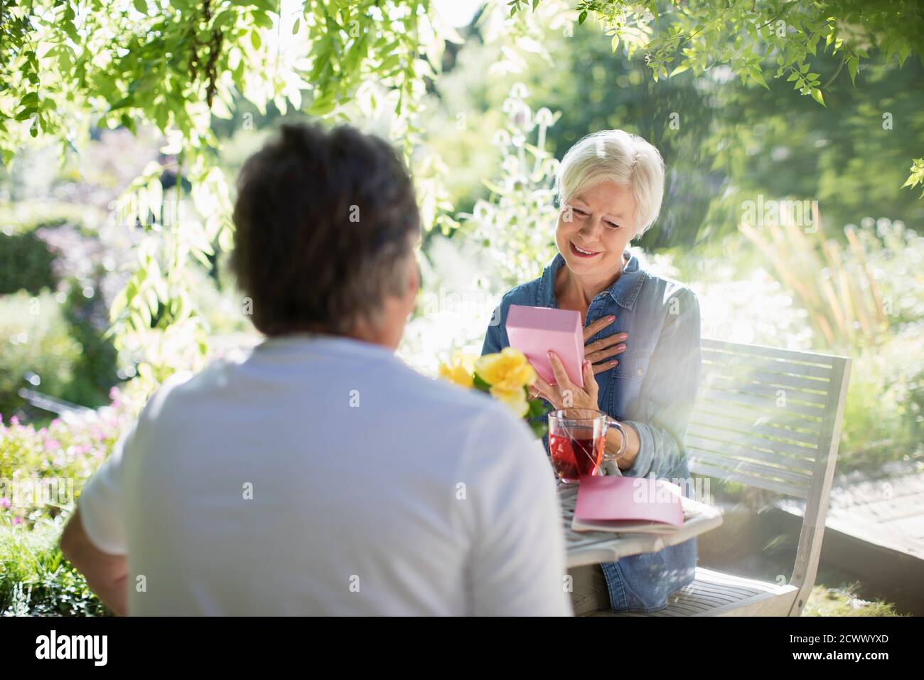 Glückliche ältere Frau Eröffnungsgeschenk von Ehemann auf sonnigen Sommer Terrasse Stockfoto