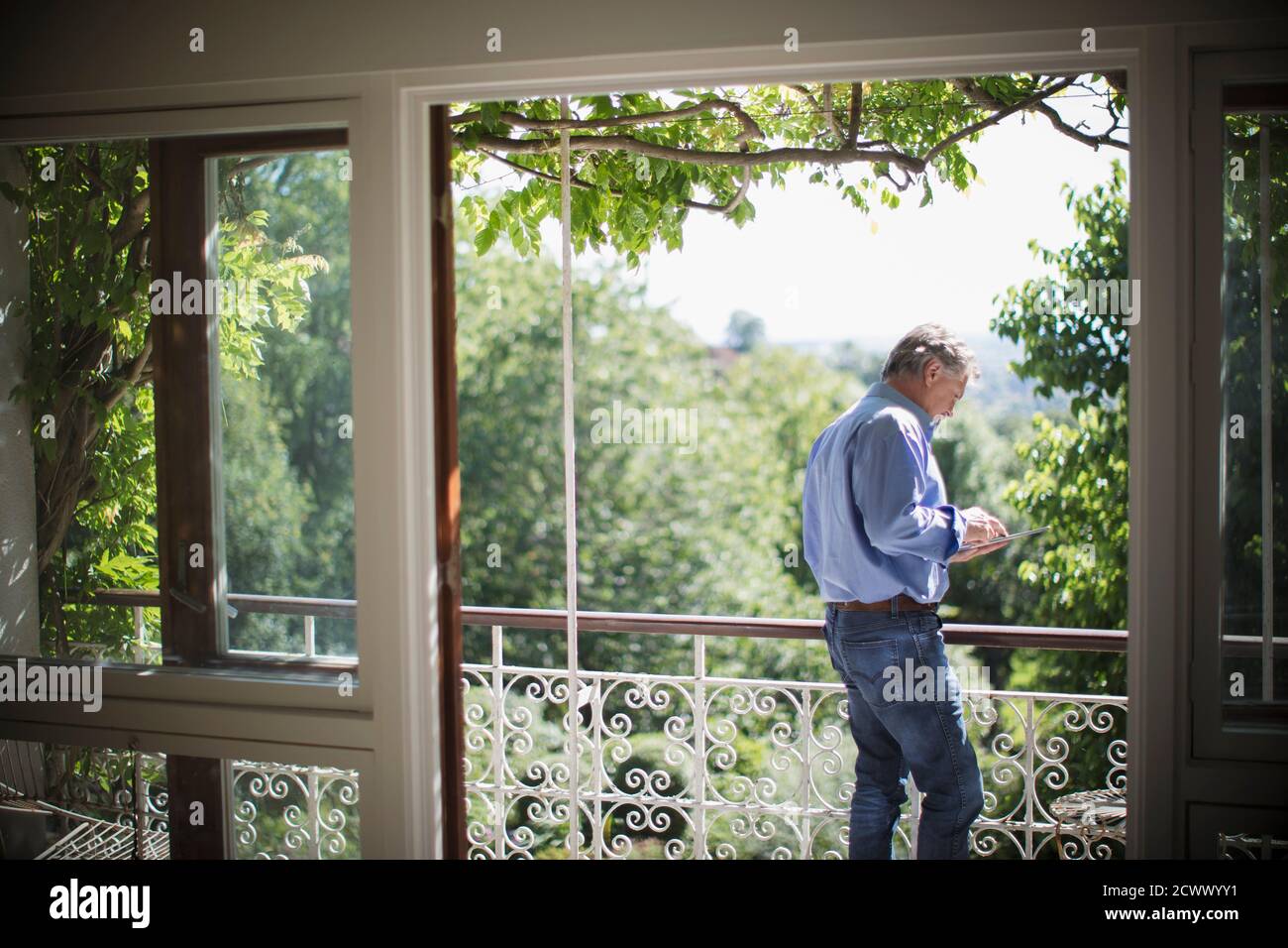 Älterer Mann mit digitalem Tablet auf sonnigem, idyllischem Balkon Stockfoto