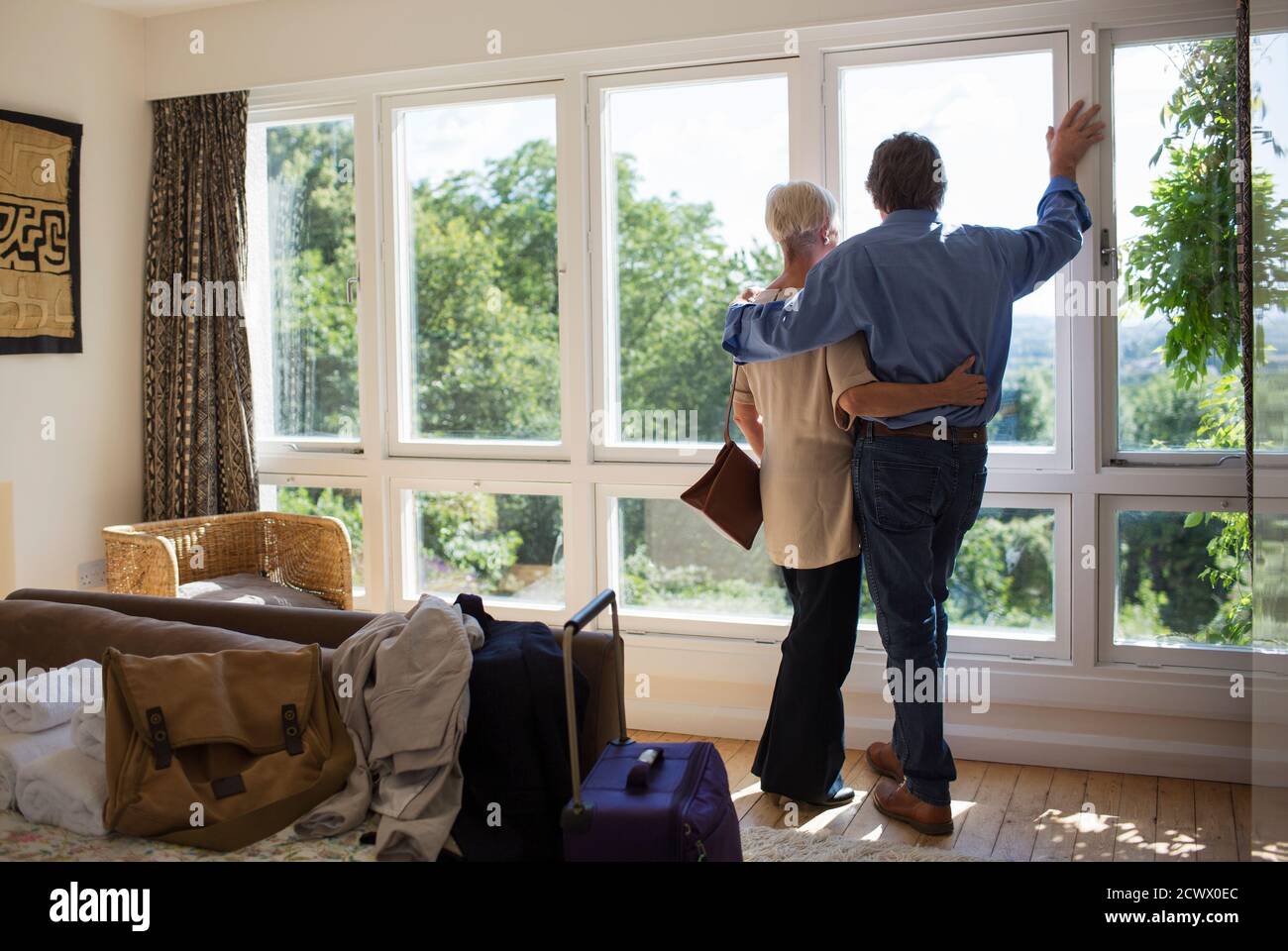 Liebevolles Senior-Paar umarmt am sonnigen Haus Vermietung Fenster Stockfoto