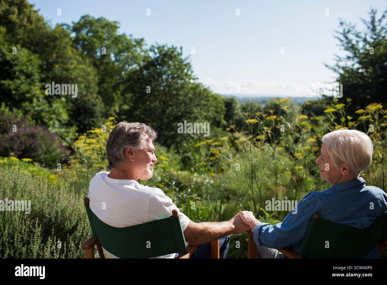 Liebevolles Seniorehepaar, das sich im sonnigen Sommergarten die Hände hält Stockfoto