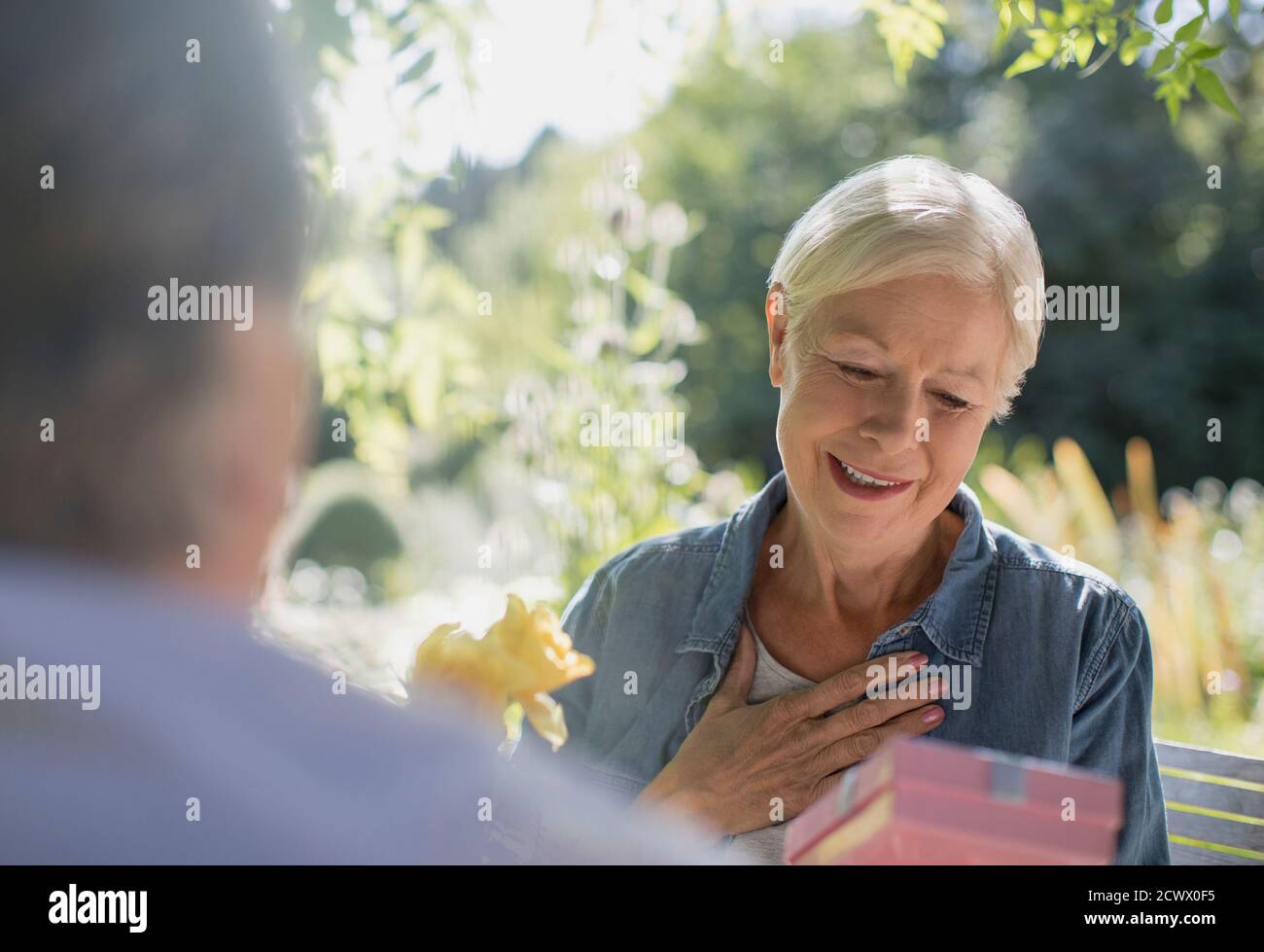 Glückliche ältere Frau, die ein Geschenk von ihrem Mann auf der sonnigen Terrasse erhielt Stockfoto