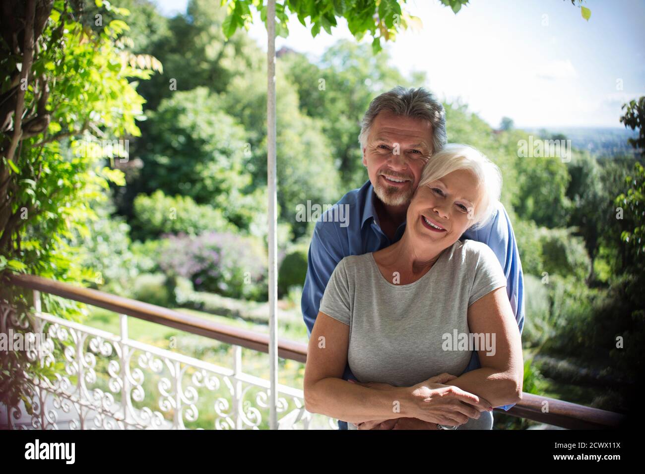 Portrait glückliches Paar umarmt auf sonnigen Sommerbalkon Stockfoto