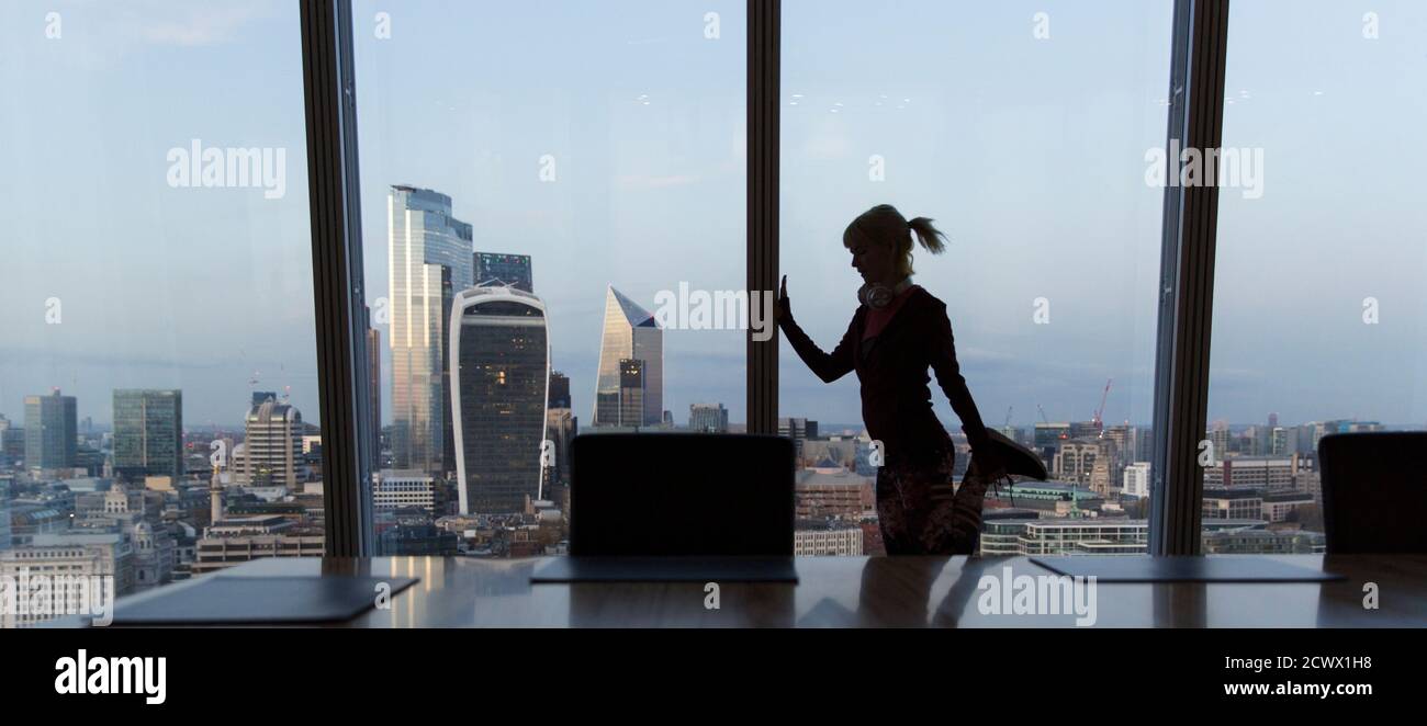 Geschäftsfrau, die sich am Bürofenster in einem Hochhaus, London, Großbritannien, ausbreitet Stockfoto