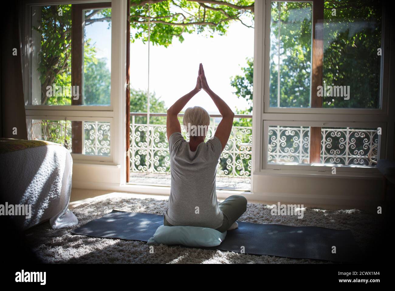 Ruhige ältere Frau praktiziert Yoga an sonnigen ruhigen Balkon Tür Stockfoto