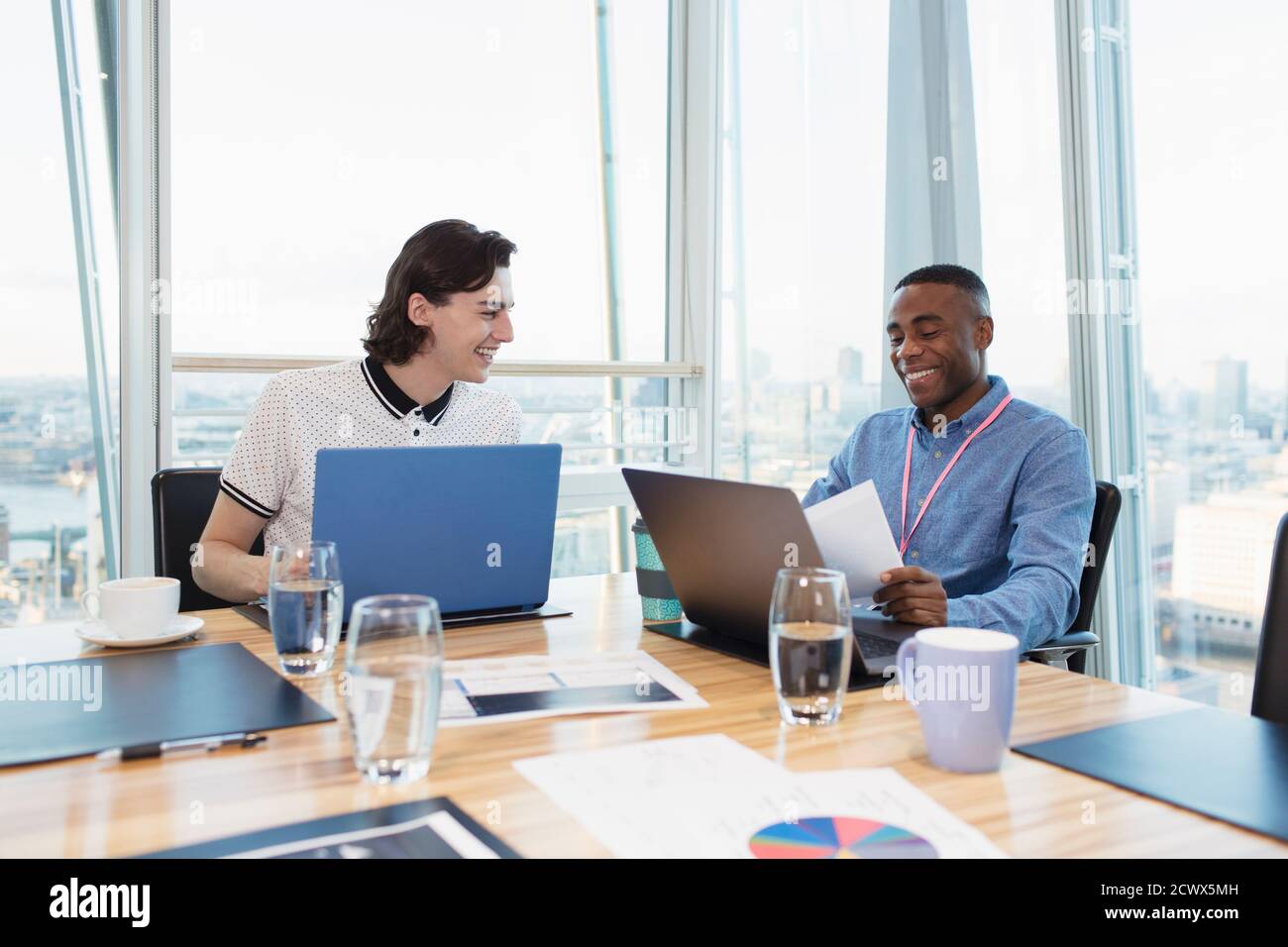 Lächelnde Geschäftsleute, die an Laptops im HochhausKonferenzraum arbeiten Stockfoto