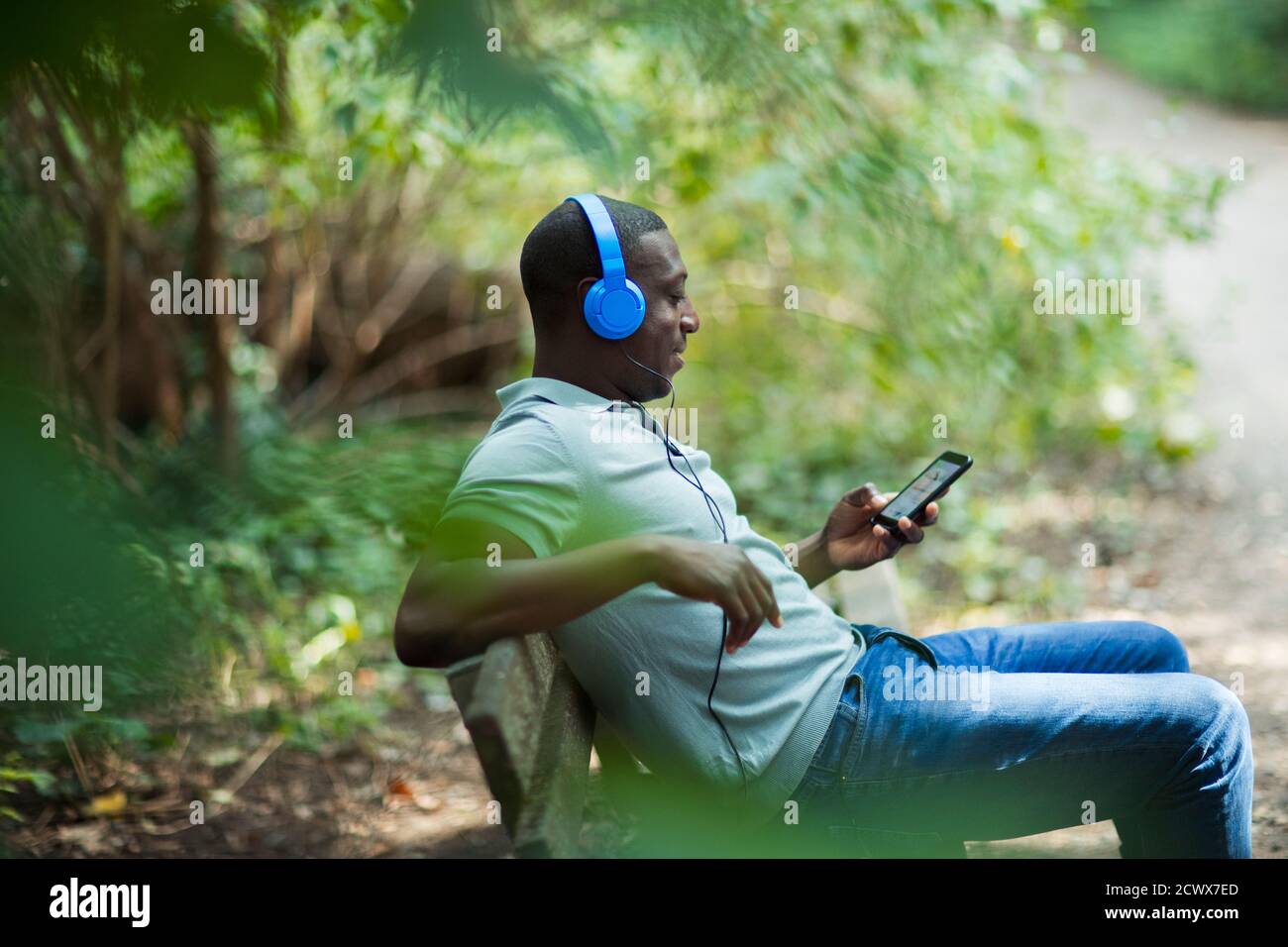 Mann entspannt auf Parkbank mit Kopfhörer und Smartphone Stockfoto