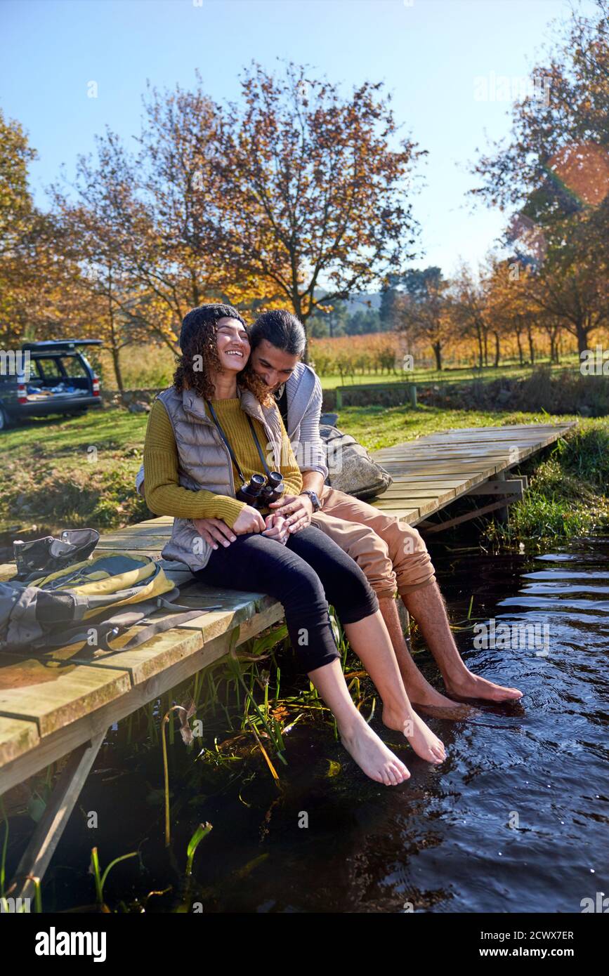 Zärtlich barfuß junges Paar lachend auf sonnigem Dock Stockfoto