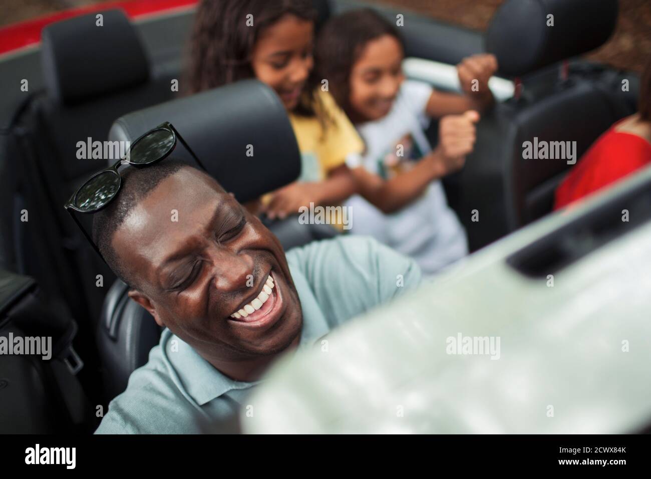 Glücklicher Mann lachend in Cabrio mit Familie Stockfoto