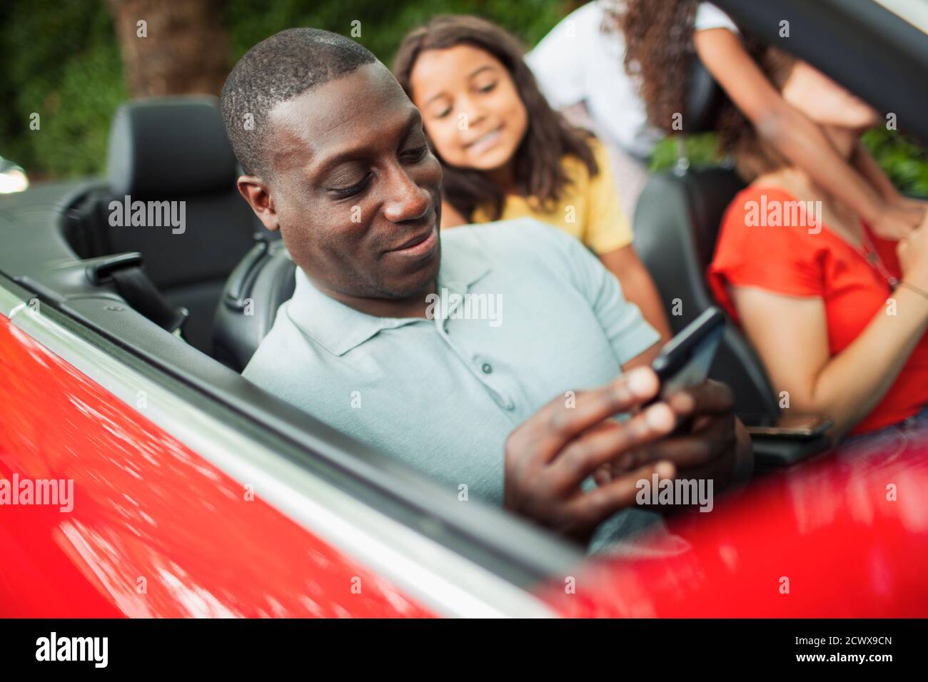 Mann mit Smartphone in Cabrio mit Familie Stockfoto