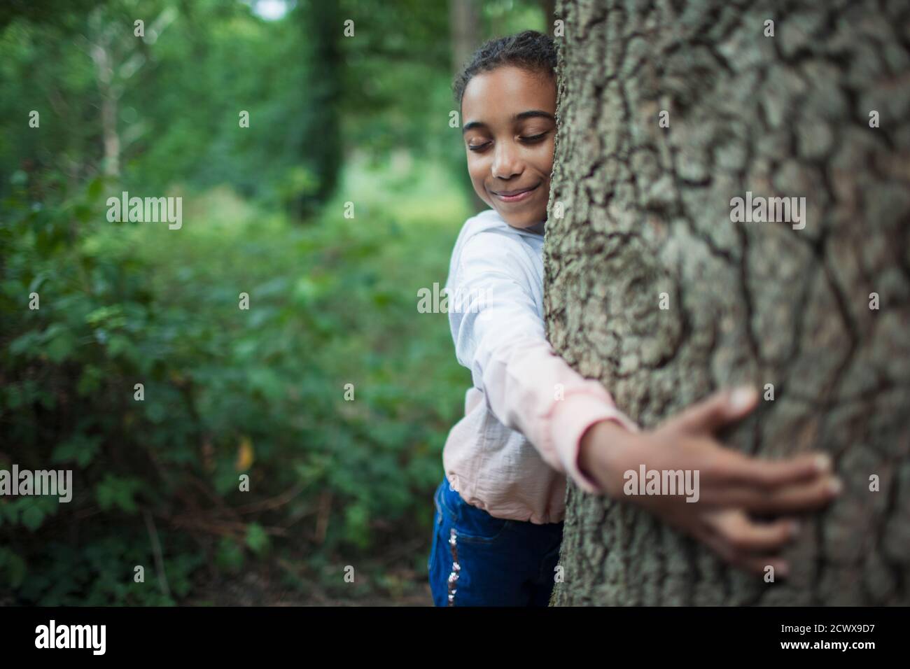 Nettes Mädchen umarmt Baumstamm in Wäldern Stockfoto