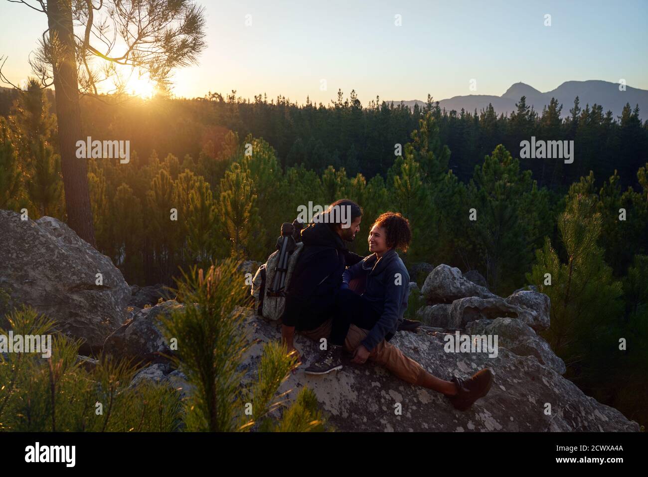 Glücklich anhänglich junges Paar entspannen auf Felsen in Wäldern an Sonnenuntergang Stockfoto