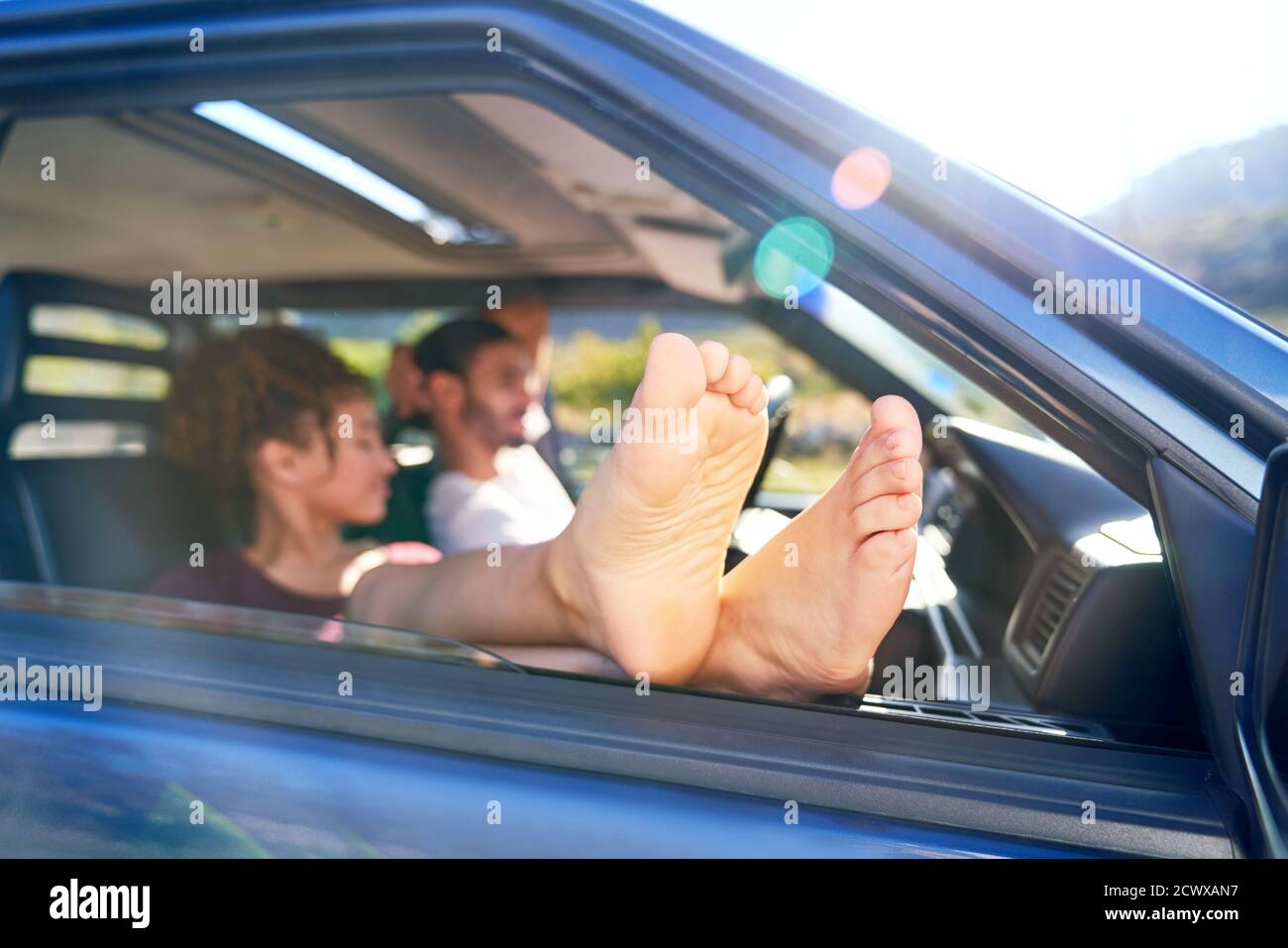 Junge Frau, die sich mit bloßen Füßen aus dem Autofenster entspannt Stockfoto