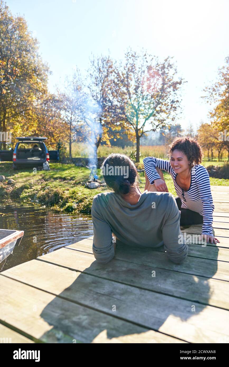 Glückliches junges Paar, das sich auf dem sonnigen Herbstdock in der Nähe des Campingplatzes entspannt Stockfoto