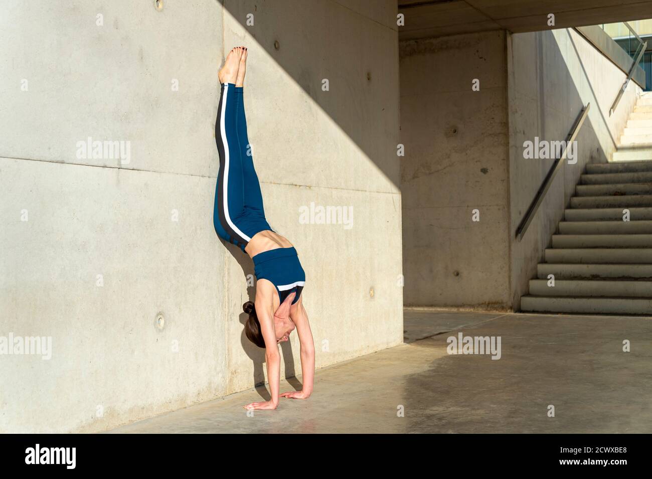 Frau, die einen Handstand gegen eine Betonwand macht, urbanes Yoga. Stockfoto