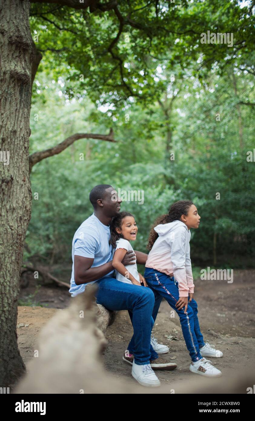 Glücklicher Vater und Töchter, die auf gefallener Baumstammte im Wald sitzen Stockfoto