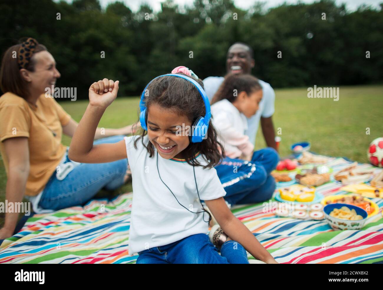 Sorgloses Mädchen, das Musik mit Kopfhörern auf der Picknickdecke hört Stockfoto