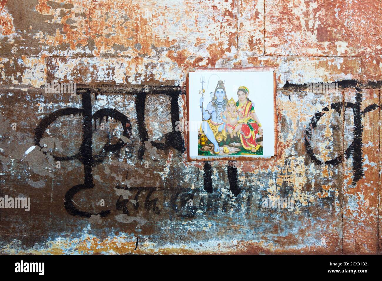 Varanasi, Uttar Pradesh, Indien : Nahaufnahme einer verwitterten Wand mit Devanagari-Schrift und einer Fliese, die die Götter Shiva, Parvati und Ganesh darstellt. Stockfoto