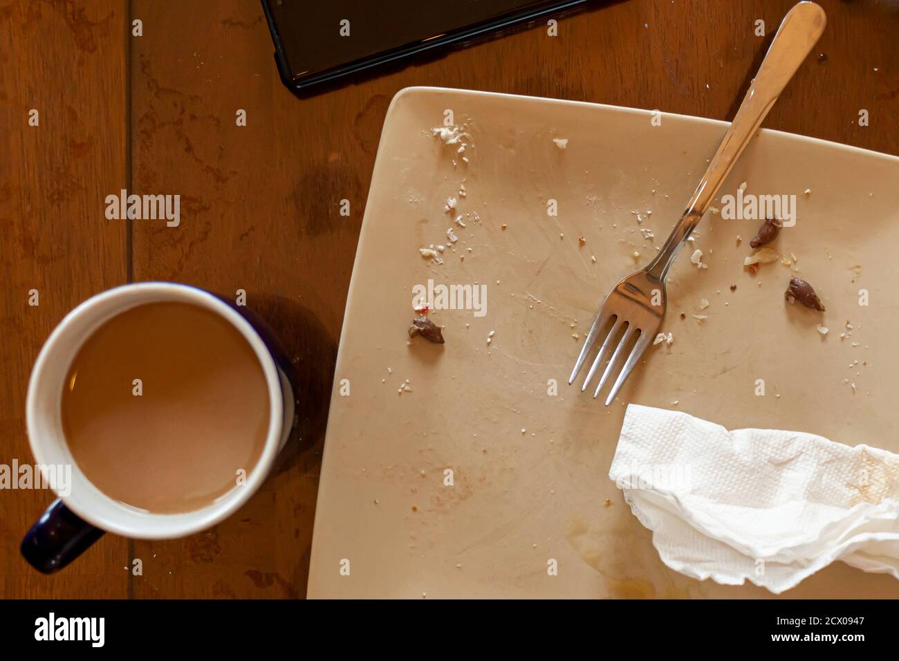 Ein flaches Bild eines Küchentisches nach einem schnellen Frühstück an einem Arbeitstag. Eine Tasse Kaffee, ein verschmierter Porzellanteller mit Olivensteinen, zerbröckelt eine Verwendung Stockfoto