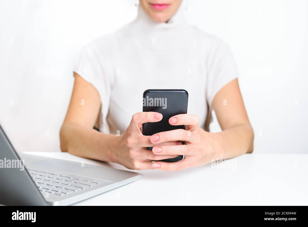 kaukasische Frau trägt weiße Kleidung mit einem Smartphone im Büro. Konzept der neuen Technologien und Ablenkung Stockfoto