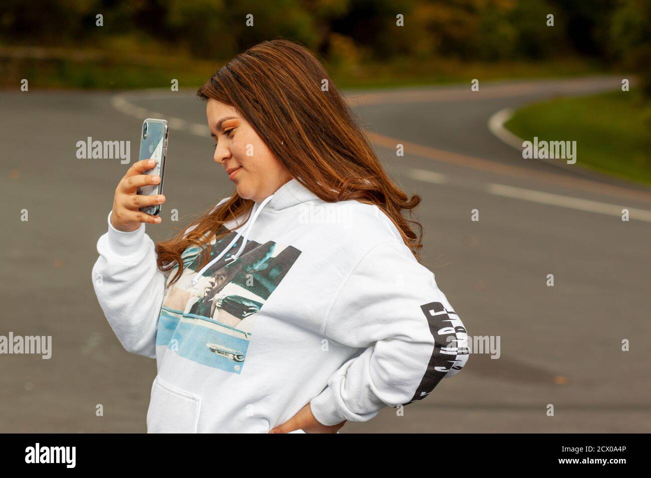 Shenandoah Valley, VA, USA 09/27/2020: Eine junge hispanische Frau mit braunem Haar im Kapuzenpullover macht ein Foto mit einem Smartphone. Sie hat ein Lächeln auf h Stockfoto