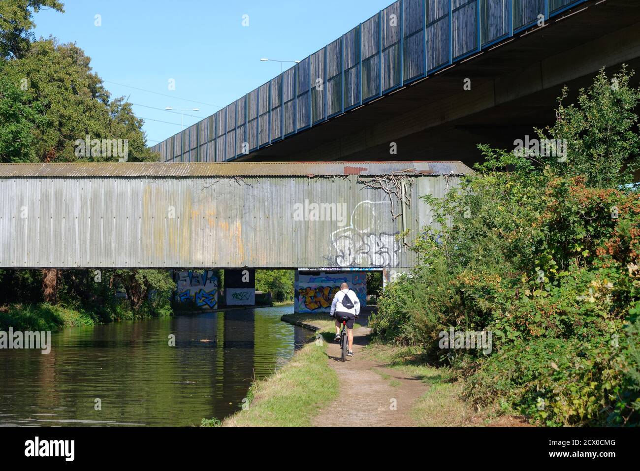 Rückansicht eines Radfahrers, der unter der M25 vorbeifährt Autobahnbrücke am Wey-Schifffahrtskanal bei New HAW Surrey England Großbritannien Stockfoto
