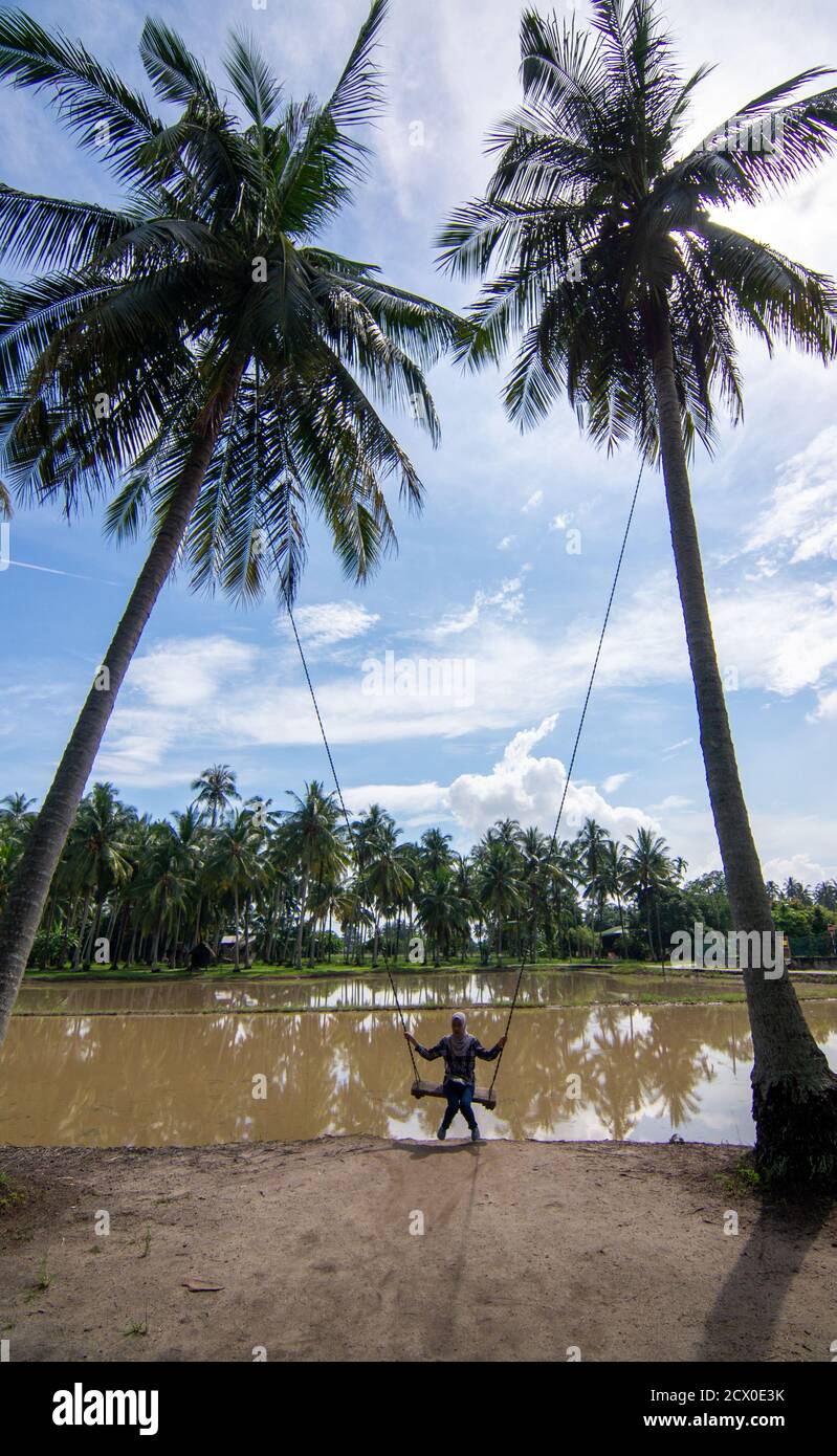 Penaga, Penang/Malaysia - Okt 27 2019: Ein Mädchen spielt Schaukel in der Kokosnussfarm. Stockfoto